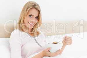 Woman in bed with a bowl of cereal in hand and a slightly raised