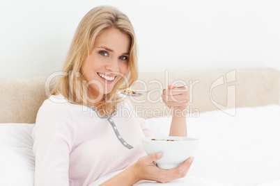 Woman in bed with a bowl of cereal in hand and a raised spoon of