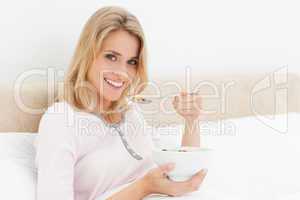 Woman in bed with a bowl of cereal in hand and a raised spoon of