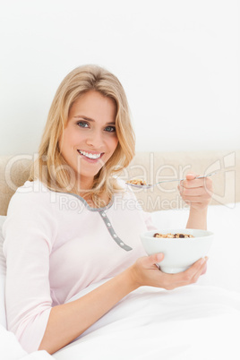 Woman with a bowl of cereal and spoon near her mouth looking ahe