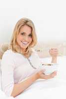 Woman with a bowl of cereal and spoon near her mouth looking ahe