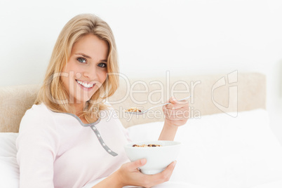 Woman in bed, with a bowl and raised spoon of cereal, smiling an