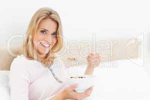 Woman in bed, with a bowl and raised spoon of cereal, smiling an
