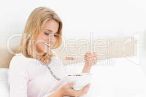 Woman in bed, with a raised spoon of cereal, looking at it and s