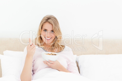 Woman in bed looking forward and smiling with a spoon and bowl o