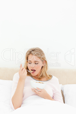 Woman in bed, about to eat a spoon of cereal with eyes closed