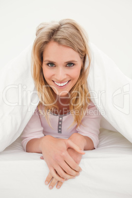 Woman in bed under a quilt, looking forward and smiling