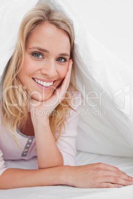 Close up, woman under the quilt smiling with her hand supporting