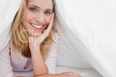 Woman under the quilt with her head on her hand as she smiles an