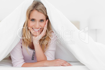 Woman under quilt, with head on hand and smiling