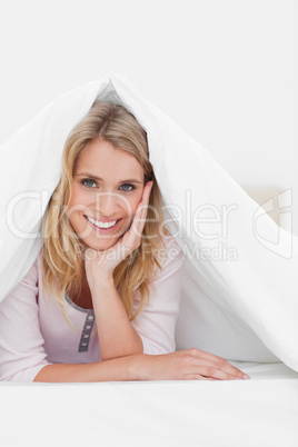 Close up, Woman under quilt with hand on head, smiling