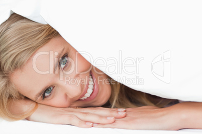 Woman lying under a quilt, covering her cheek as she smiles