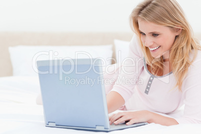 Woman lying on the bed, using a laptop and smiling