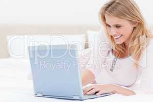 Woman lying on the bed, using a laptop and smiling