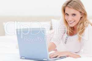 Woman lying on the bed, with laptop, looking forward and smiling