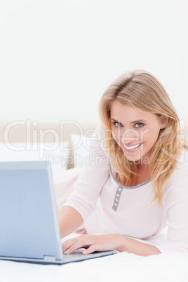 Woman lying on the bed, with a laptop, while looking forward and