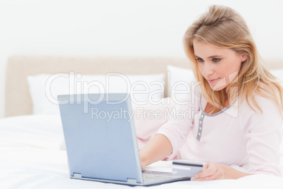 Woman lying on a bed with her laptop, looking at the screen