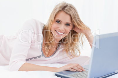 Woman lying on the bed, with her laptop, while looking forward a