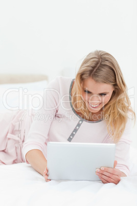 Woman lying across the bed, tablet pc in hand and smiling