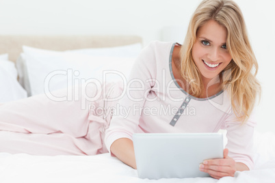 Woman lying on the bed with tablet pc in hand, looking up and sm