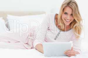 Woman lying on the bed with tablet pc in hand, looking up and sm