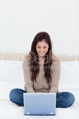 Woman looking at her laptop, while on the bed with crossed legs