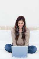 Woman looking at her laptop, while on the bed with crossed legs