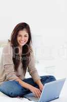 Woman smiling as she looks sideways, with her laptop on the bed