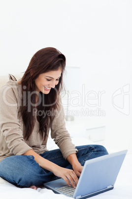 Woman smiling as she uses her laptop on her bed