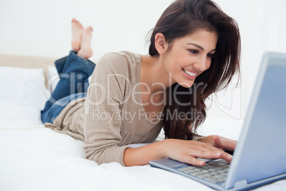 Woman lying down the bed with her laptop in front of her and smi