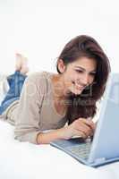 Close up, woman lying on the bed smiling with her laptop in fron