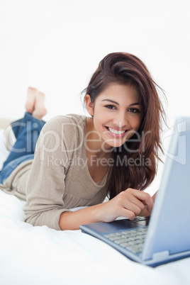 Woman smiling in front of her laptop, lying on the bed with her