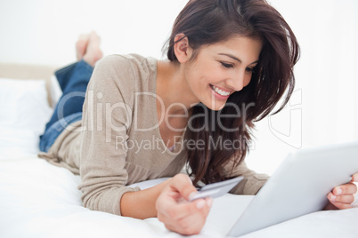 Woman using a tablet with her credit card, and smiling while lyi