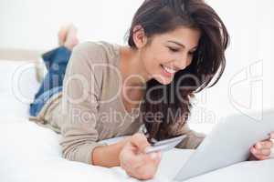 Woman using a tablet with her credit card, and smiling while lyi