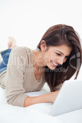 Woman smiling as she uses her tablet while lying on the bed