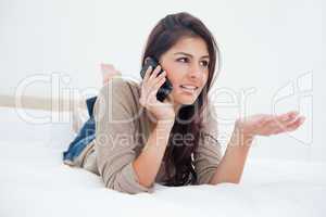 Woman making a phonecall glancing to the side as she lies on the