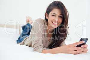 Woman lying on the bed, her phone in her hands as she smiles and