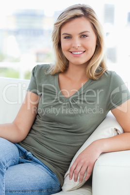 Woman looking ahead, smiling and resting her arm on the couch ar