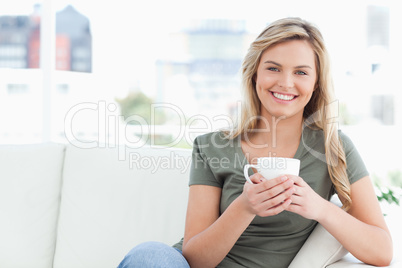 Woman smiling, holding a cup in hands and sitting on the couch