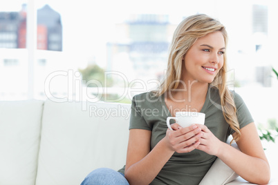 Woman holding a cup, sitting on the couch, looking sideways and