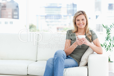 Woman sitting in the corneer of the couch, smiling with cup in h