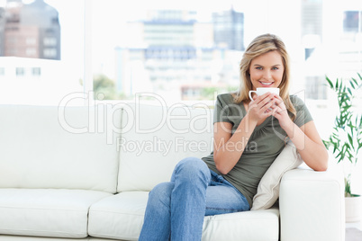 Woman smiling with a cup near her lips, sitting on the couch and