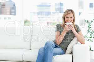 Woman smiling with a cup near her lips, sitting on the couch and