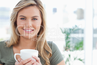 Woman holding a mug in her hands and smiling, while looking forw