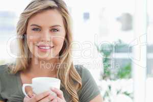 Woman holding a mug in her hands and smiling, while looking forw