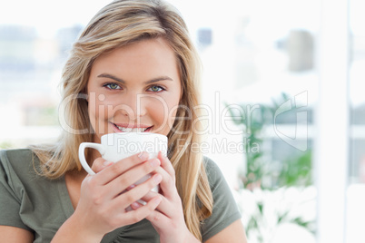 Woman looking forward, smiling with a mug up to near her mouth