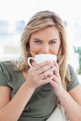 Close up, woman with a mug held up in front of her mouth and loo