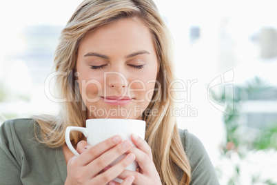 Woman with mug raised to near her mouth, eyes closed and smiling