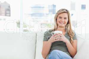 Woman sitting on couch, smiling and holding a cup in front of he
