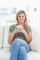 Centered shot, woman sitting on the couch with a cup in hands an